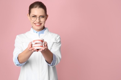 Female dentist holding jaws model on color background. Space for text