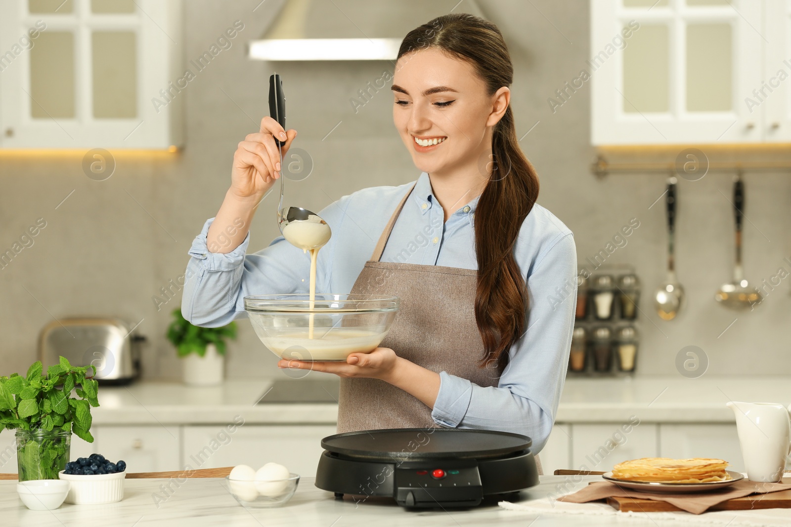 Photo of Happy woman with dough for crepes at white marble table in kitchen