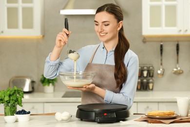 Photo of Happy woman with dough for crepes at white marble table in kitchen