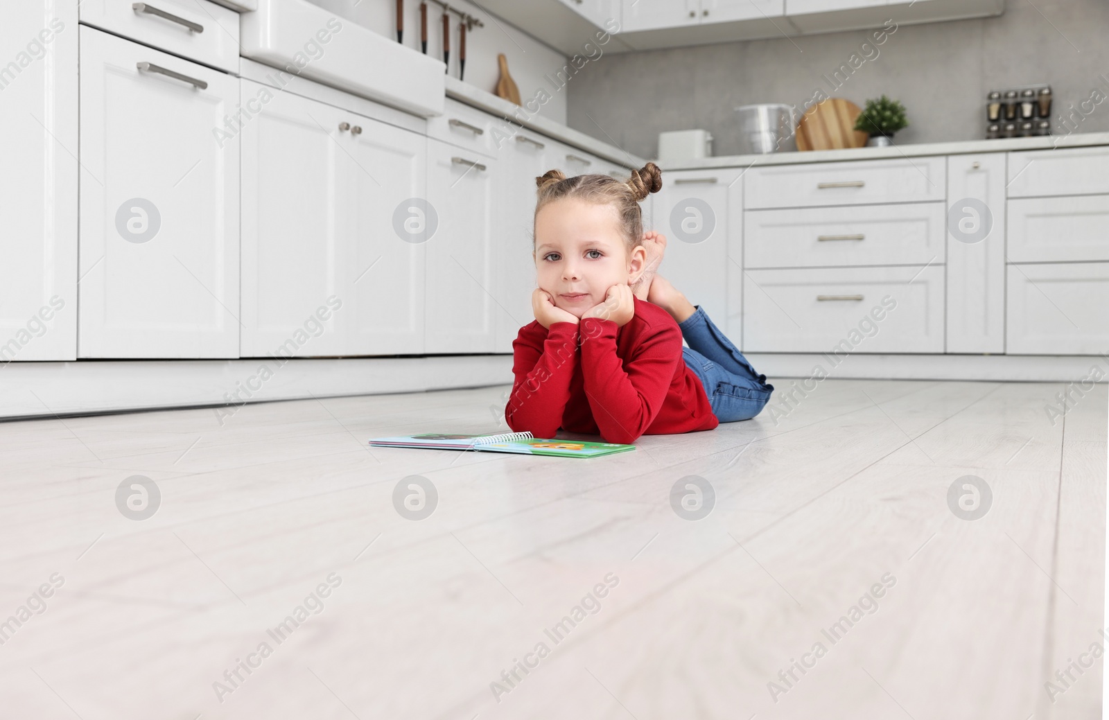 Photo of Cute little girl with book on warm floor in kitchen. Heating system