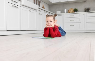 Photo of Cute little girl with book on warm floor in kitchen. Heating system