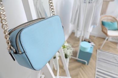 Elegant light blue handbag hanging on rack in dressing room