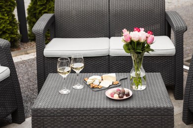 Photo of Vase with roses, glasses of wine and food on rattan table on outdoor terrace