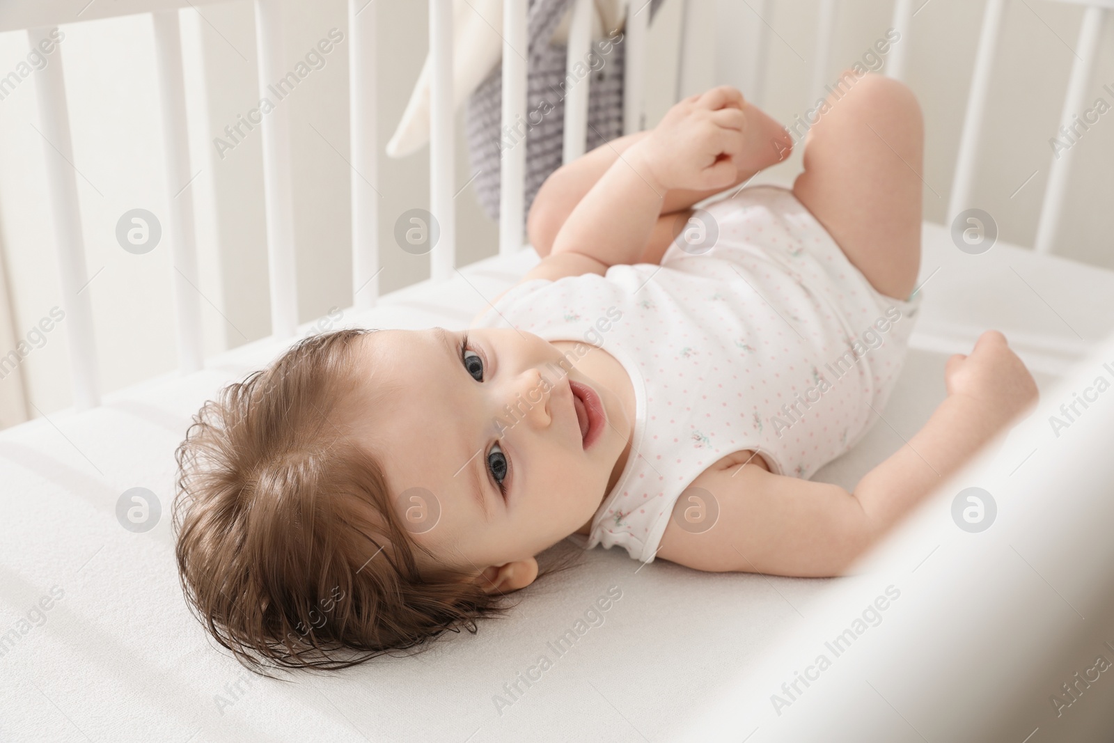 Photo of Cute little baby lying in comfortable crib at home