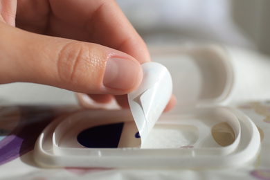 Photo of Woman opening pack of wet wipes against blurred background, closeup