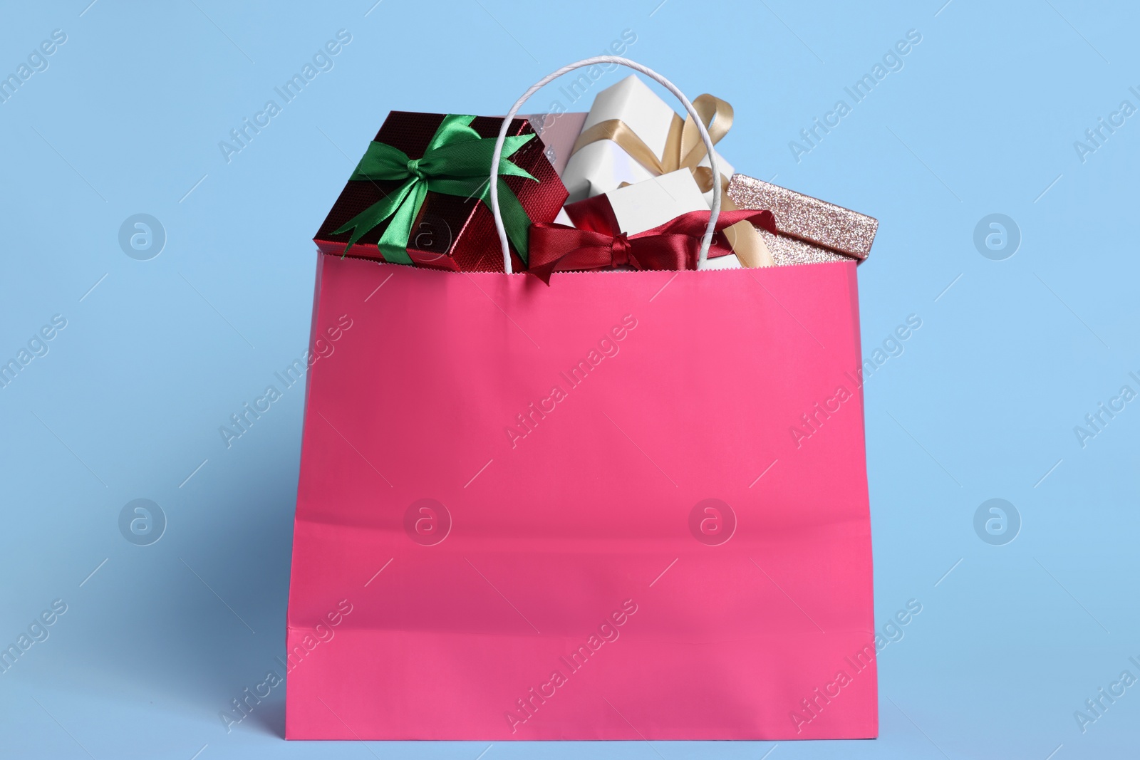 Photo of Pink paper shopping bag full of gift boxes on light blue background