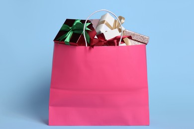 Pink paper shopping bag full of gift boxes on light blue background
