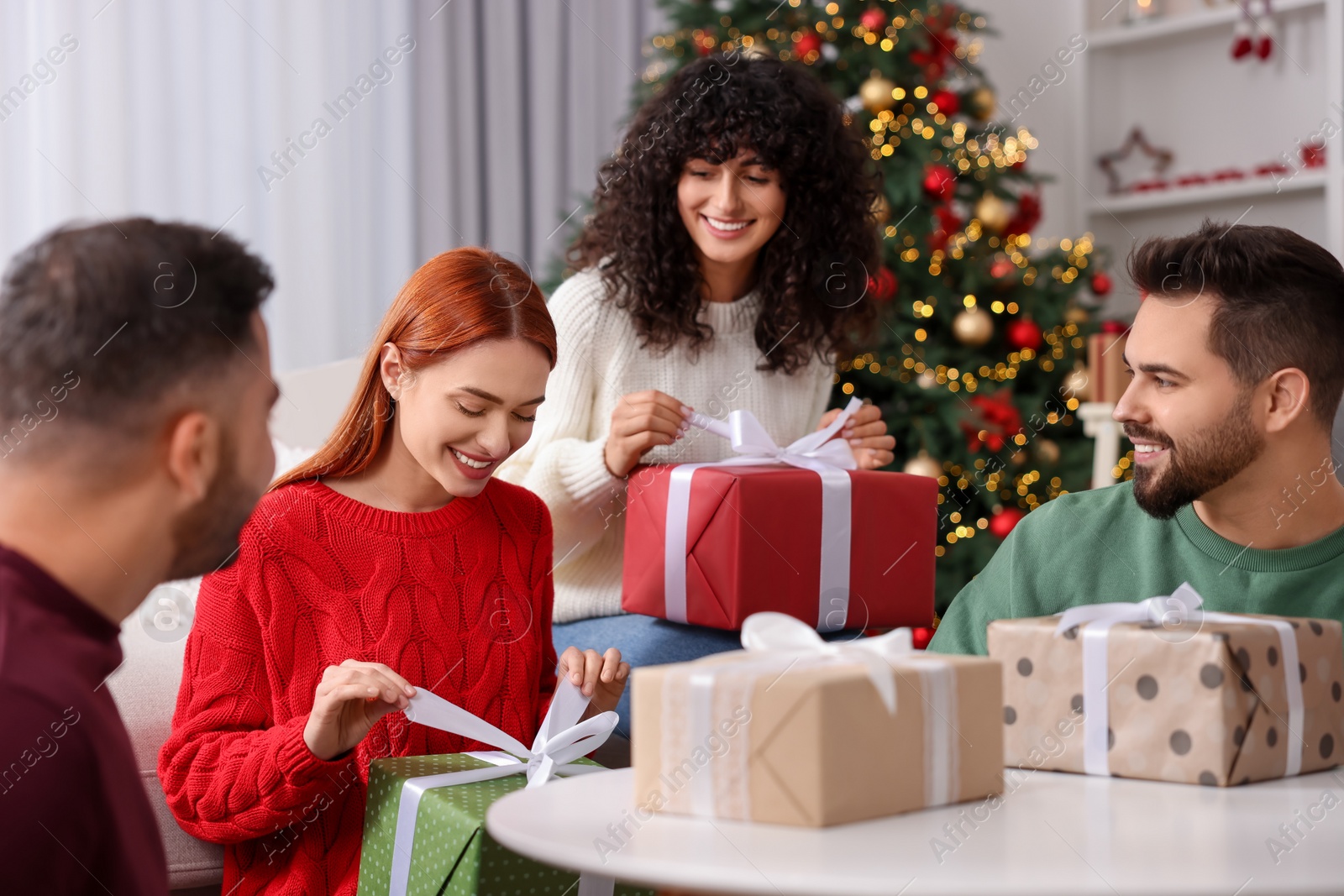 Photo of Christmas celebration in circle of friends. Happy women opening gifts at home