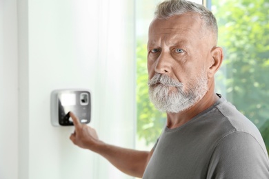 Photo of Mature man entering code on alarm system keypad indoors