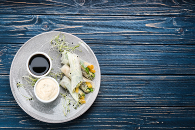 Photo of Delicious rolls wrapped in rice paper served on blue wooden table, top view. Space for text