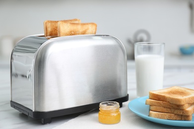 Photo of Modern toaster with slices of bread, honey and milk on white table in kitchen