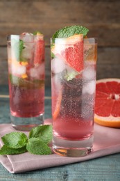 Photo of Delicious grapefruit lemonade with soda water and mint on blue wooden table. Fresh summer cocktail