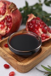 Photo of Tasty pomegranate sauce in bowl and fruits on light table, closeup