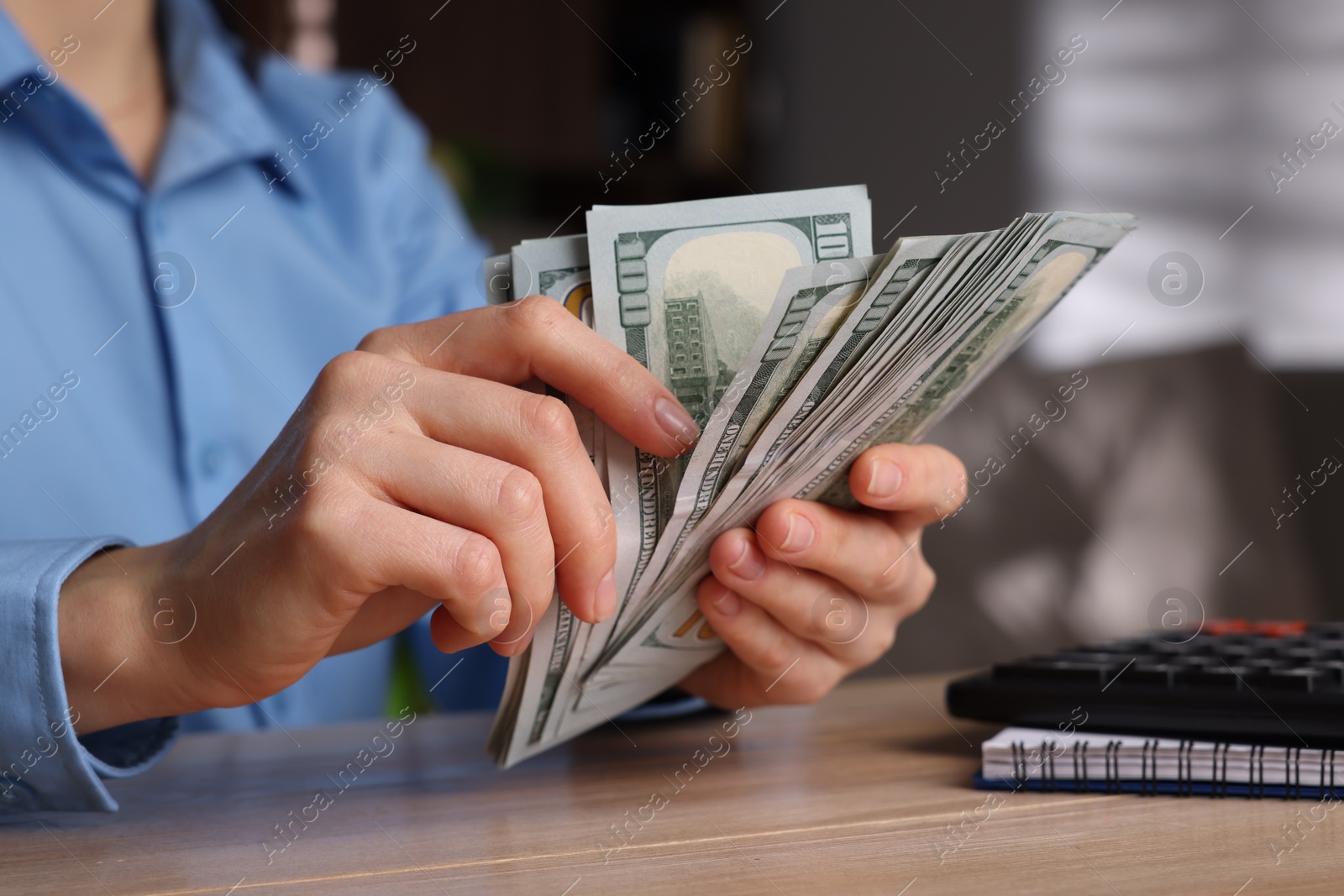 Photo of Money exchange. Woman counting dollar banknotes at wooden table, closeup