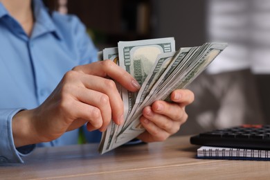 Money exchange. Woman counting dollar banknotes at wooden table, closeup