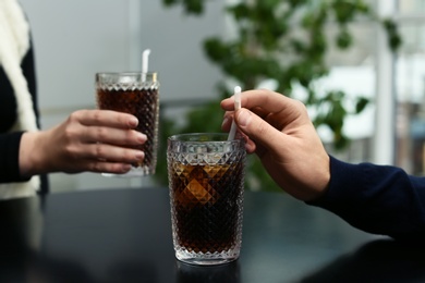 Photo of Couple with glasses of cold cola at table in cafe, closeup