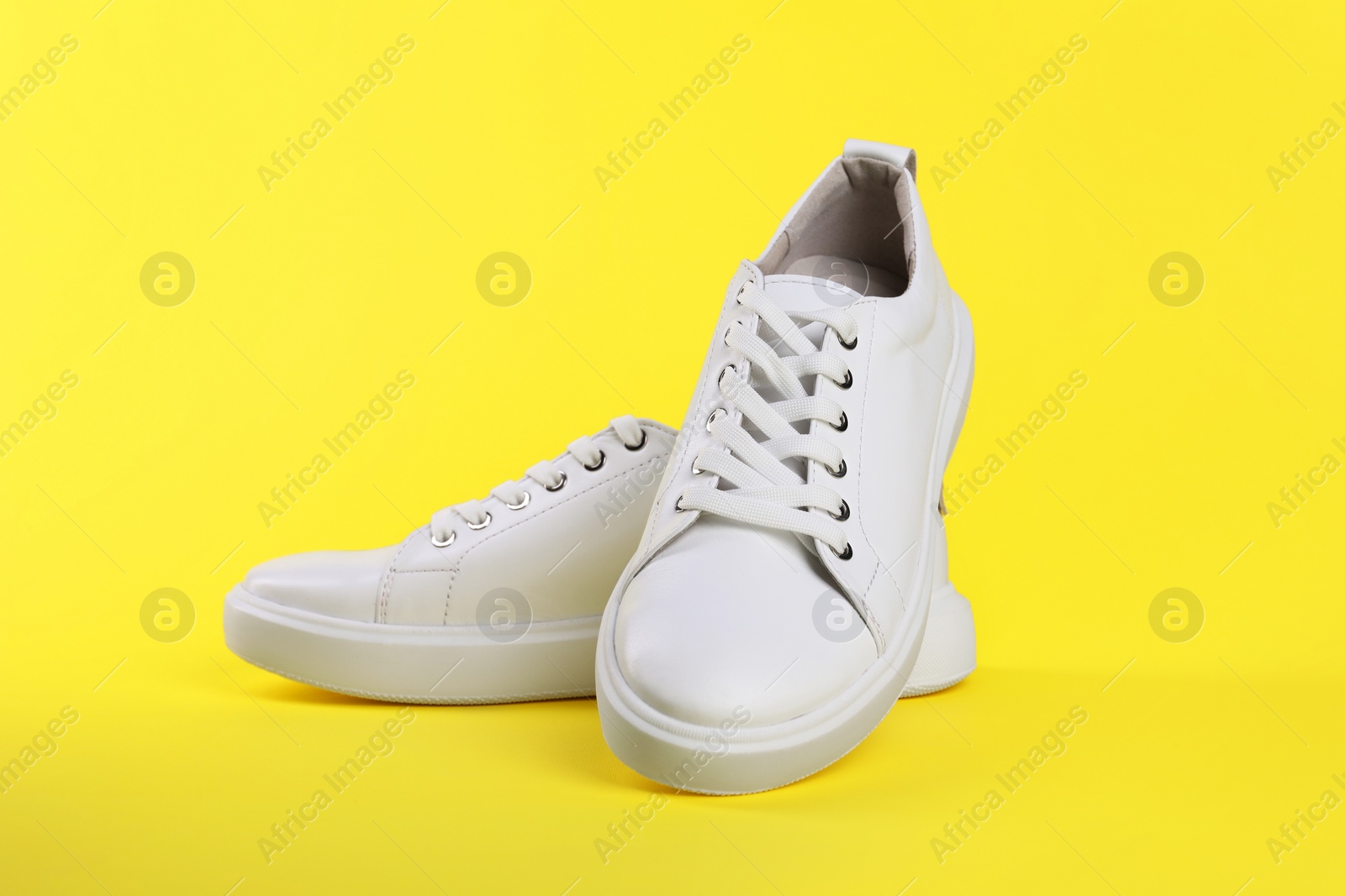 Photo of Pair of stylish white sneakers on yellow background