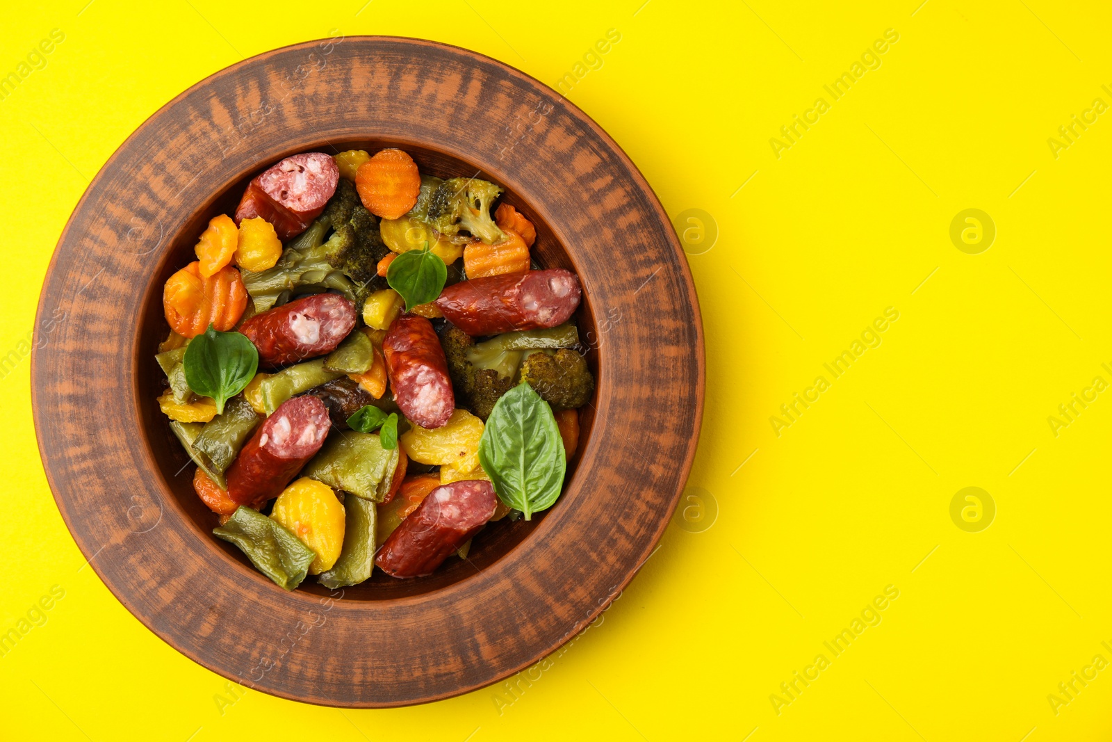 Photo of Delicious sausage and baked vegetables on yellow background, top view. Space for text