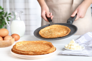 Photo of Woman cooking delicious thin pancakes at white wooden table