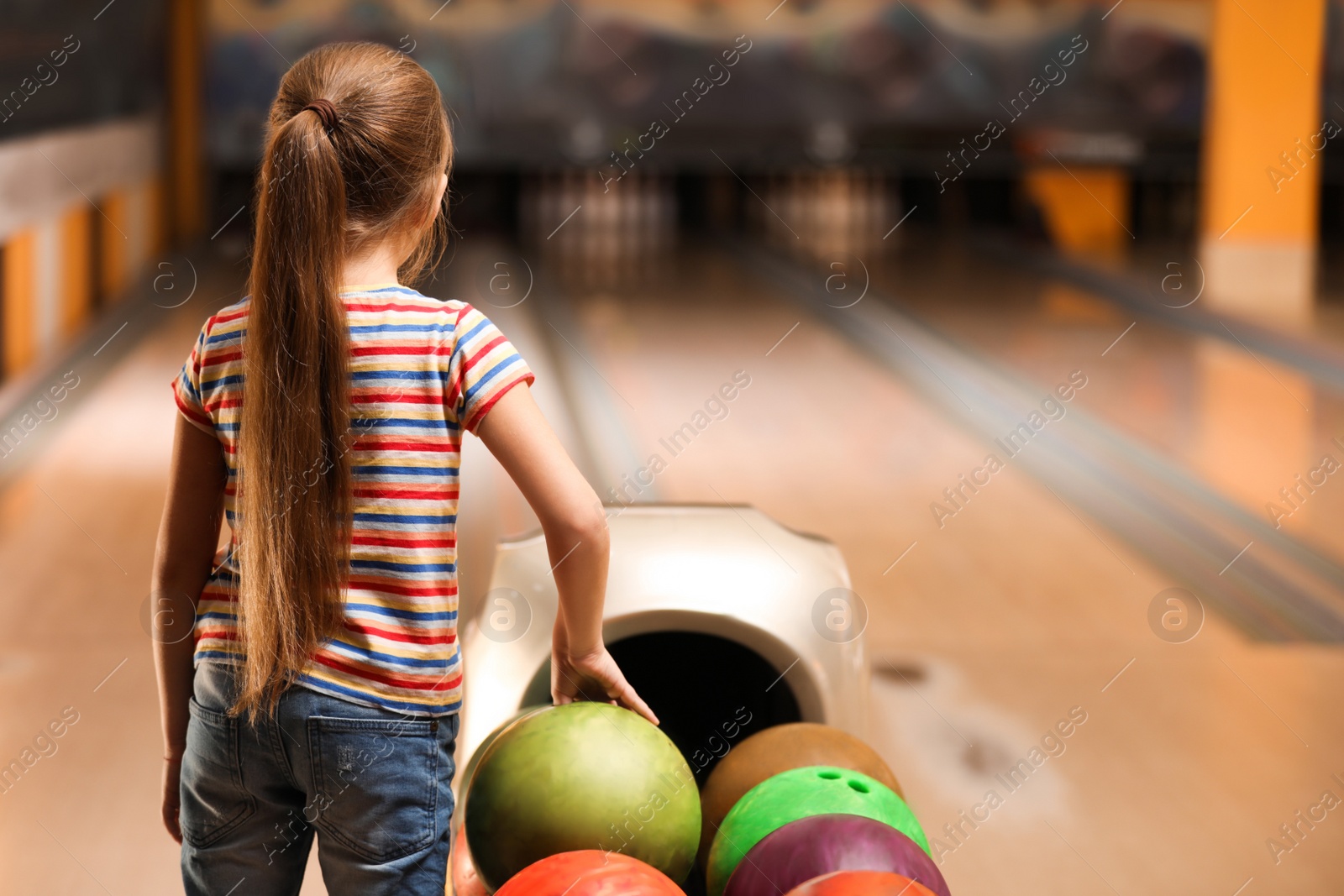 Photo of Little girl near balls in bowling club. Space for text