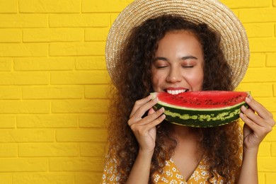Photo of Beautiful young African American woman eating watermelon near yellow brick wall. Space for text