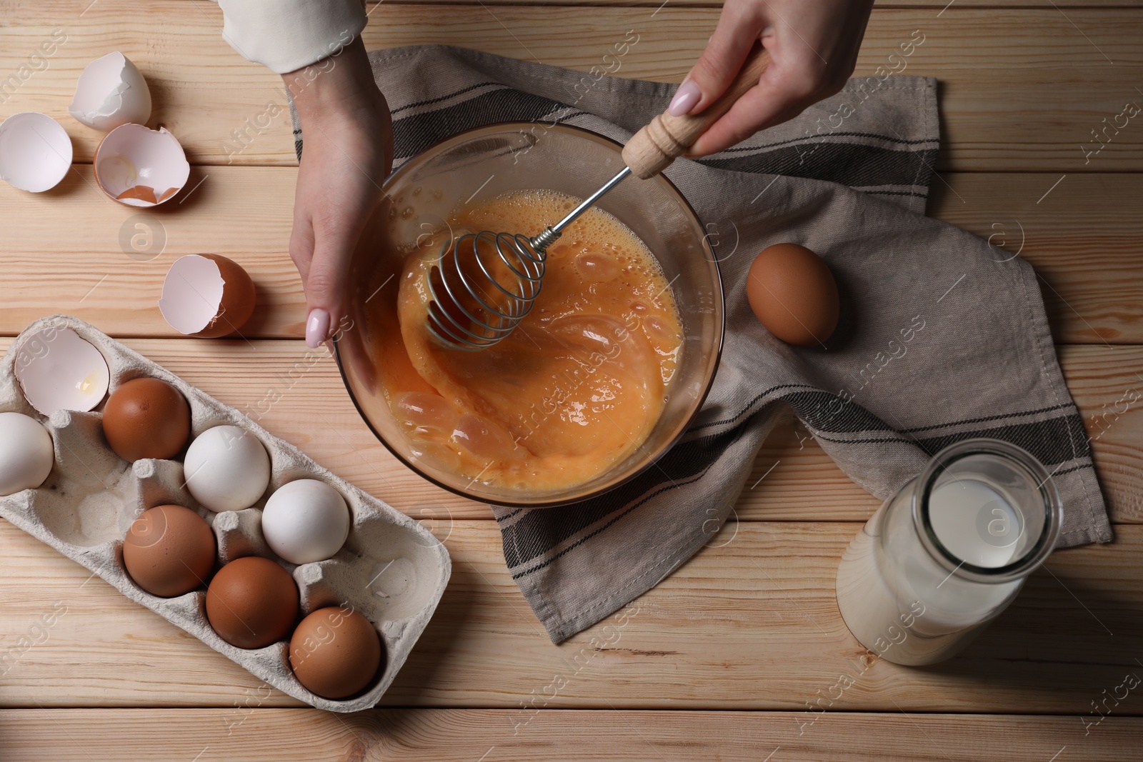 Photo of Woman whisking eggs in bowl at wooden table, top view