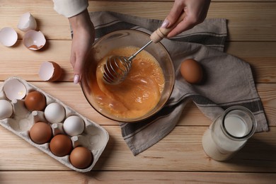 Woman whisking eggs in bowl at wooden table, top view