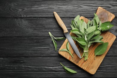 Photo of Bunch of fresh sage leaves and knife on black wooden table, flat lay. Space for text