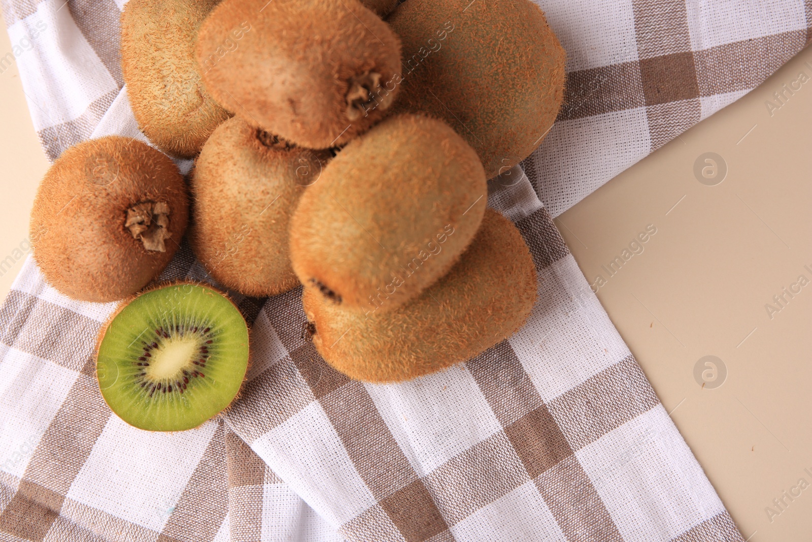 Photo of Heap of whole and cut fresh kiwis on beige table, top view. Space for text
