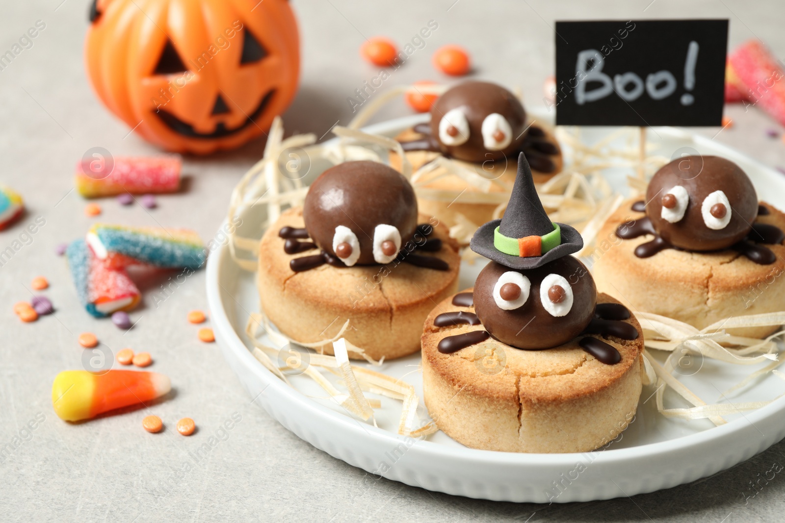 Photo of Delicious biscuits with chocolate spiders on light grey table, closeup. Halloween celebration