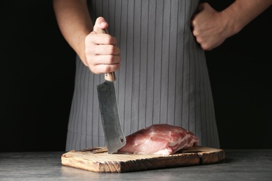 Photo of Man cooking fresh raw meat on table against dark background, closeup
