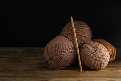 Soft  woolen yarns and knitting needle on wooden table against dark background, space for text