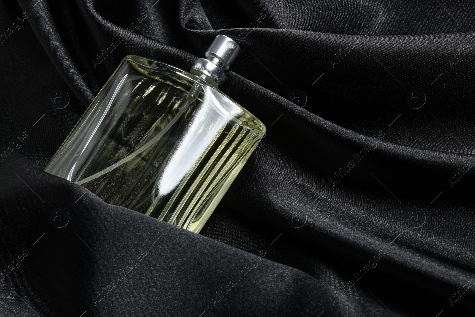 Photo of Luxury men's perfume in bottle on black satin fabric, space for text