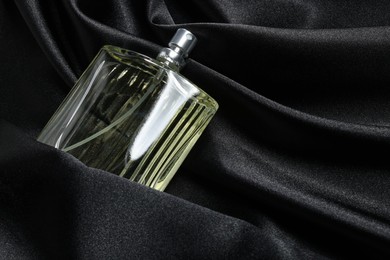 Photo of Luxury men's perfume in bottle on black satin fabric, space for text