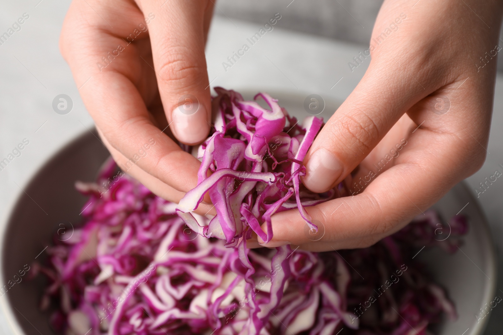 Photo of Woman holding shredded fresh red cabbage at grey table, closeup