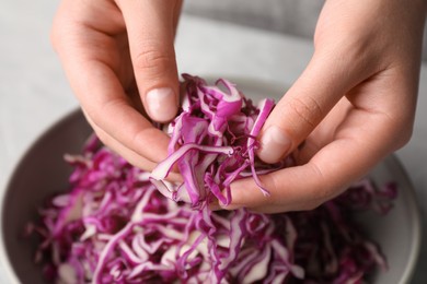 Photo of Woman holding shredded fresh red cabbage at grey table, closeup
