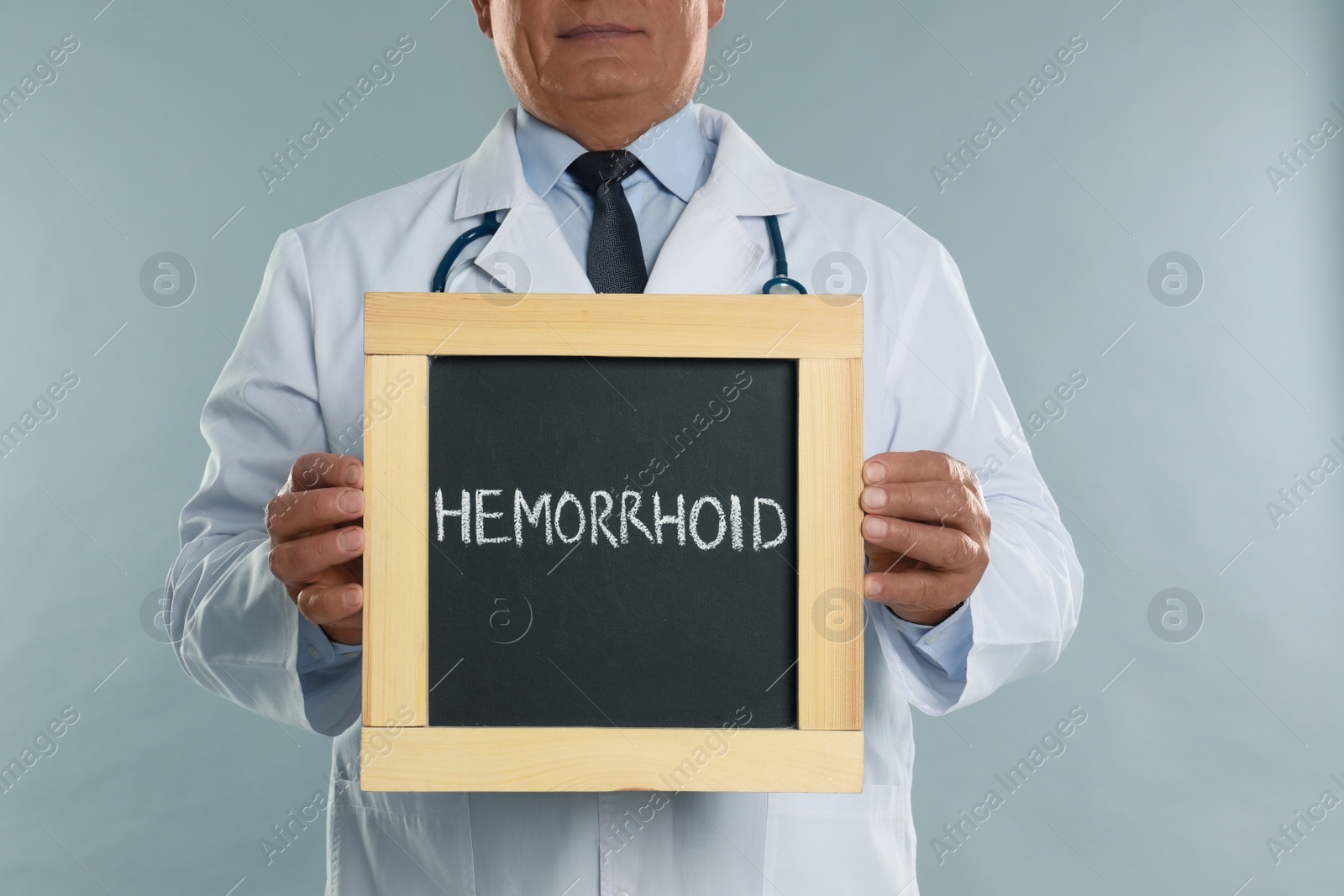 Photo of Doctor holding blackboard with word HEMORRHOID on light grey background, closeup