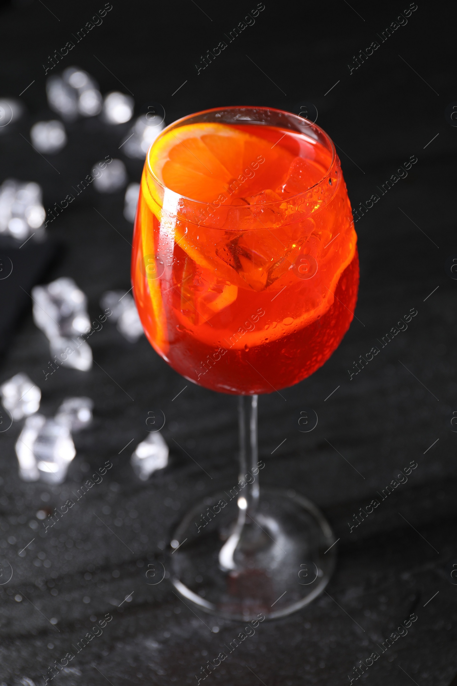 Photo of Glass of tasty Aperol spritz cocktail with ice cubes on dark gray table