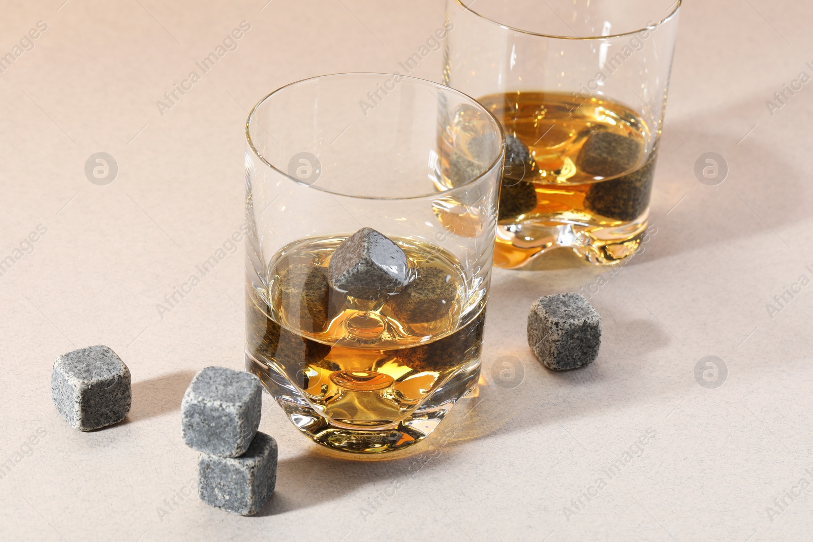 Photo of Whiskey stones and drink in glasses on light table, closeup