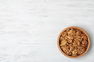 Tasty walnuts in bowl and space for text on wooden background, top view