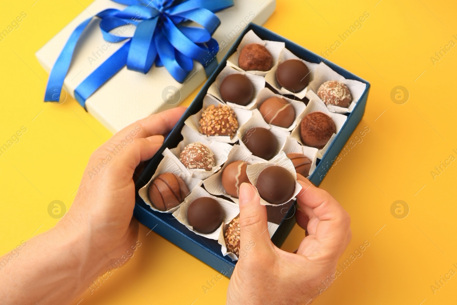 Photo of Woman taking chocolate candy from box on yellow background, closeup