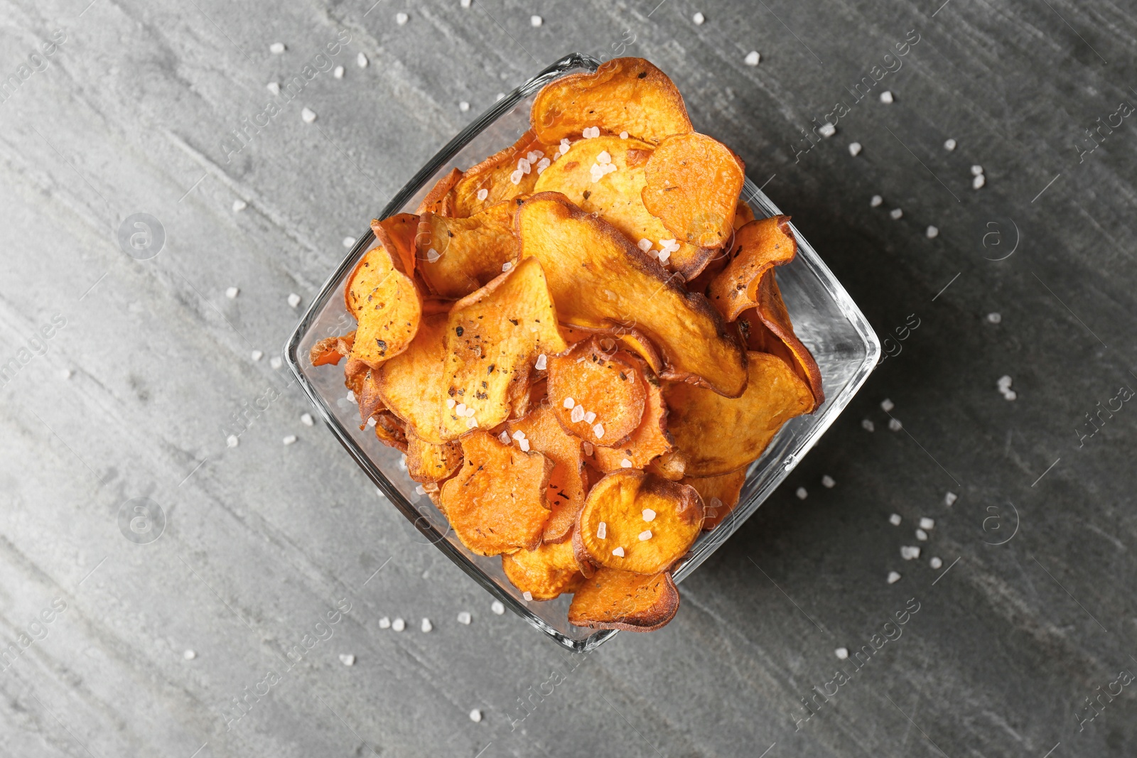Photo of Bowl of sweet potato chips and salt on grey table, top view