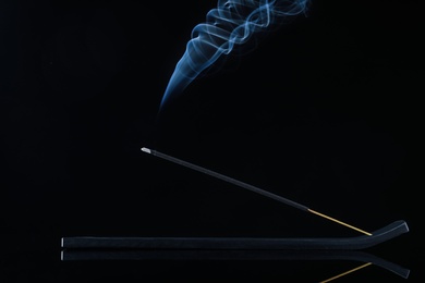 Photo of Incense stick smoldering in holder on black background