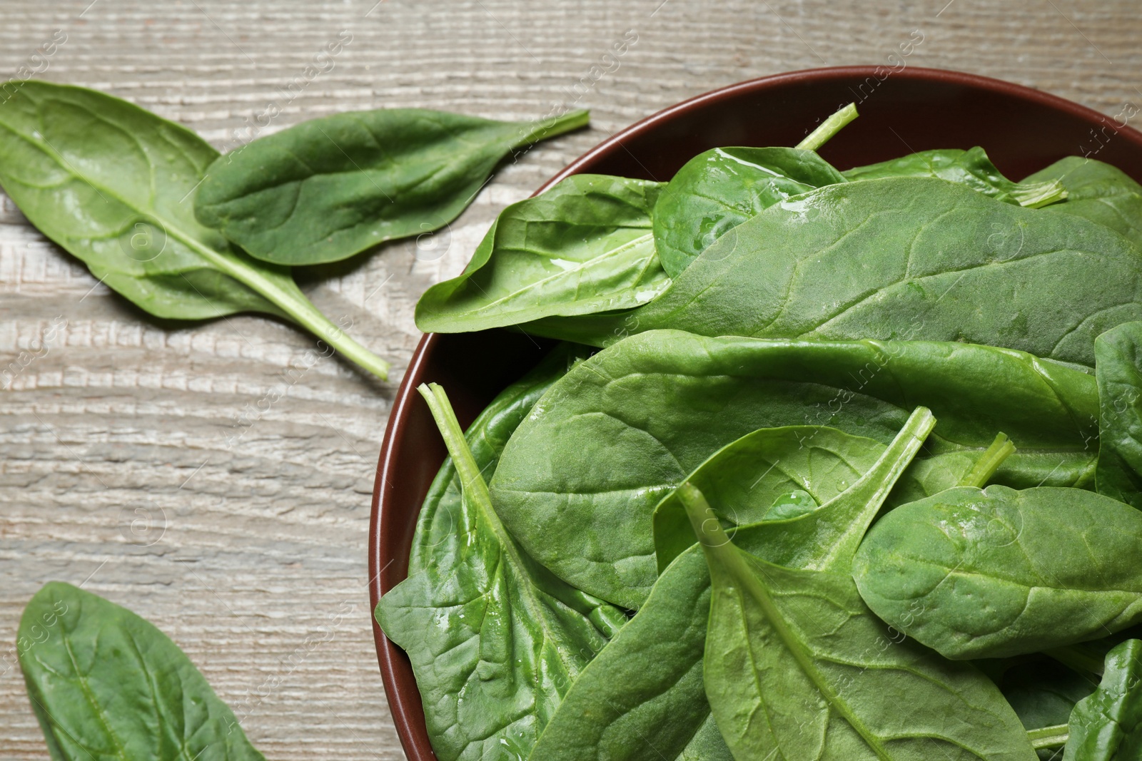 Photo of Bowl with fresh green healthy spinach on wooden table, top view