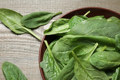 Bowl with fresh green healthy spinach on wooden table, top view