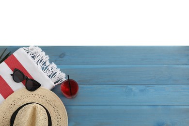 Light blue wooden surface with beach towel, straw hat, refreshing drink and sunglasses on white background, top view. Space for text