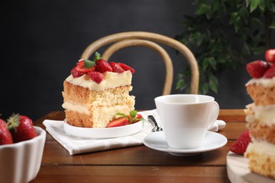 Piece of tasty cake with fresh strawberries, mint and cup of tea on wooden table