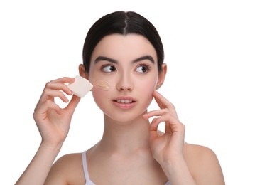 Teenage girl applying foundation on face with makeup sponge against white background