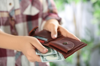 Photo of Woman putting money into wallet on blurred background, closeup