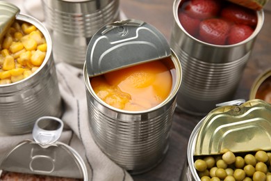 Photo of Open tin cans with peaches and different products on wooden table, closeup